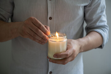 Man holding a burning candle in his hands, elegant young man with candle jar, meditation and mindfulness concept