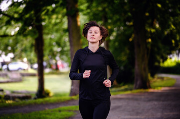 A young woman in athletic wear jogging on a forest trail, surrounded by lush green trees. Capturing a healthy lifestyle and outdoor fitness.