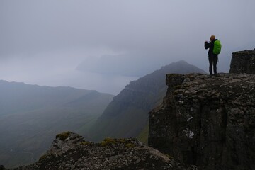 Obraz premium Silhouette of person on peak on foggy day. Eysturoy Island and climbing highest peak of Faroe Islands - Slættaratindur, Denmark. 
