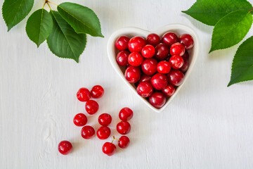 Cherries in a white heart-shaped bowl on a white wooden surface