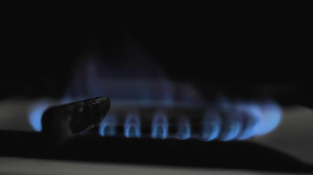 A lit burner on a gas hob close-up with a blue flame. Gas burning in a kitchen cooker in a dark room