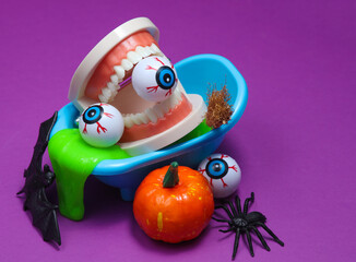 Obraz premium Halloween still life of toy bath with jaw, eyeballs and slime, bat and spider, witches broom, pumpkin on purple background