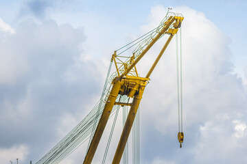 Large yellow industrial crane with cables against a cloudy sky.
