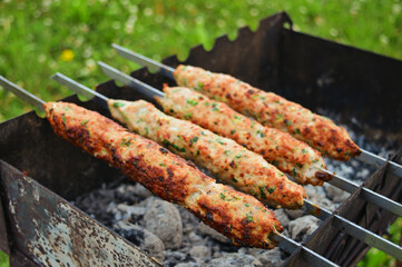 Kebab lula kebab on skewers on a charcoal barbecue grill and fire underneath.