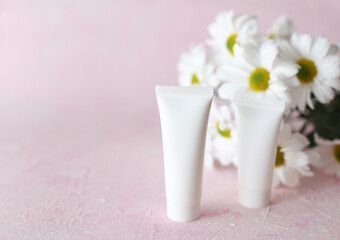 White tubes of cream with a bouquet of flowers on a pink background