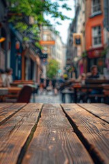 Fototapeta premium A wooden table in the foreground with a blurred background of an urban street cafe. The background features outdoor seating, pedestrians walking by, street art on nearby buildings.