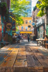 Fototapeta premium A wooden table in the foreground with a blurred background of an urban street cafe. The background features outdoor seating, pedestrians walking by, street art on nearby buildings.