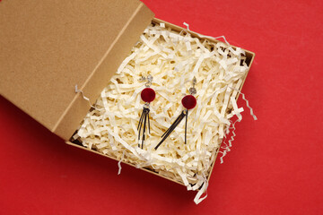 Earrings in craft box with filler on red background. Product packing