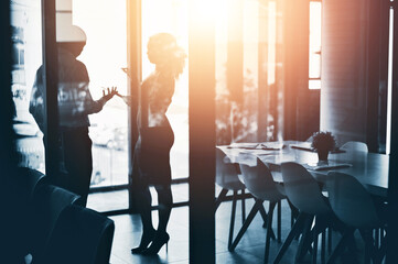 Business people, meeting and discussion with team in boardroom for morning at office. Businessman and woman discussing project, proposal or ideas with silhouette, glare or lens flare at workplace