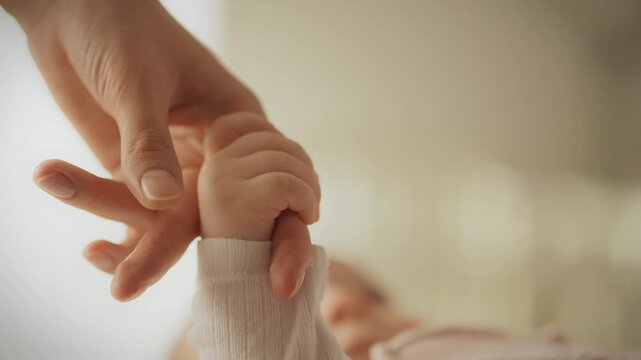 The baby's tiny hand squeezes his mother's finger, reflecting the mother's love and care. The child seeks mother’s affection and warmth for a sense of security