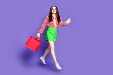Full size photo of pretty young girl walking shopping bags jump wear trendy pink outfit isolated on purple color background