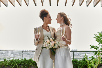 Two brides toast each other with champagne at their rooftop wedding ceremony.