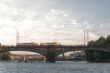 Fototapeta premium Trams crossing a bridge over the Vltava river in Prague while rowers enjoy the water. Czech Republic