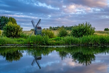 Obraz premium Dutch windmill, green fields, beautiful evening sky, clouds reflecting in the water.