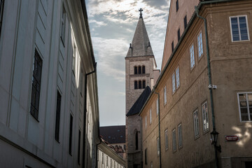 St. George's Basilica tower rising above buildings in a narrow street of Prague, Czech Republic