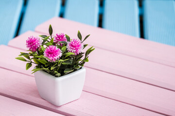 Artificial colorful flowers in decorative flowerpots on blue and pink wooden background