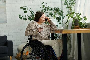 A young woman in a wheelchair sits at a table in her home, talking on her phone.