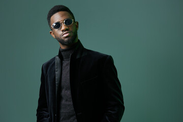 Obraz premium Stylish man in sunglasses and black turtleneck standing confidently against a vibrant green background