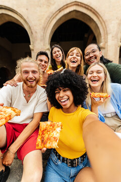 Portrait group of diverse friends taking selfie photo eating pizza at city. Smiling multiracial young people having fun enjoying summer vacation in Italy. Travel and friendship concept.