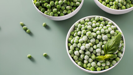 Three white bowls filled with frozen green peas on green background.