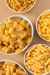 Raw pasta variety in bowls on brown background upper view