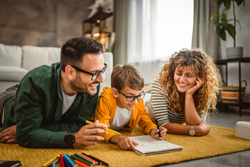 Family of three lie down on the carpet and draw at home together