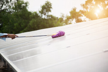 Man using a mop and water to clean the solar panels that are dirty with dust and birds' droppings to improve the efficiency of solar energy storage.