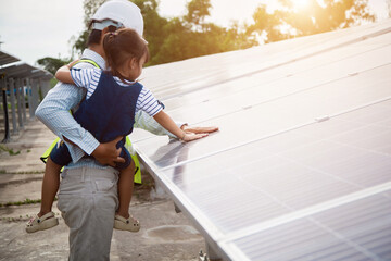 Rear view of dad holding her little girl in arms and showing at their house with installed solar panels. Alternative energy, saving resources and sustainable 