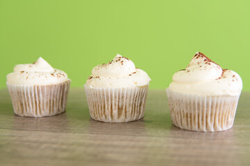 Three cupcakes with whipped cream and chocolate sprinkles on top. on green wooden background
