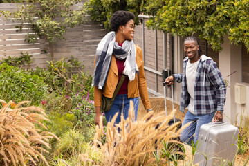 African American couple arriving home, carrying luggage and smiling outdoors