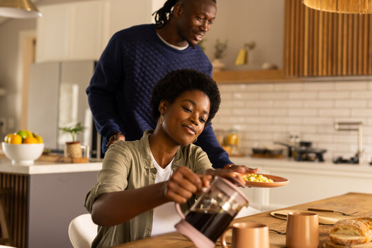 At home, African American couple enjoying breakfast, woman pouring coffee in kitchen