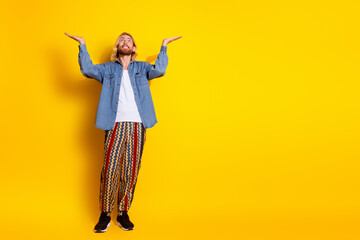 Full body photo of attractive young man hold look up empty space dressed stylish denim clothes isolated on yellow color background