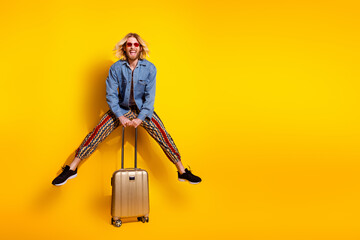 Obraz premium Full length photo of handsome young male suitcase traveler jumping dressed stylish denim garment isolated on yellow color background