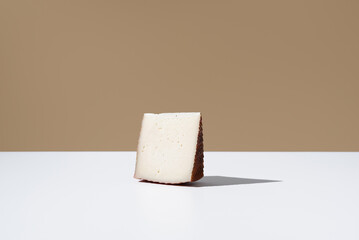 Trozo de queso de cabra curado. Aperitivo español en una mesa blanca y fondo marrón	
