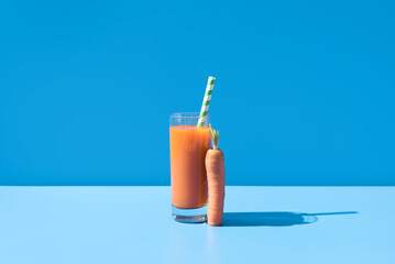 Jugo de zanahoria en un vaso transparente con pajita  sobre fondo azul