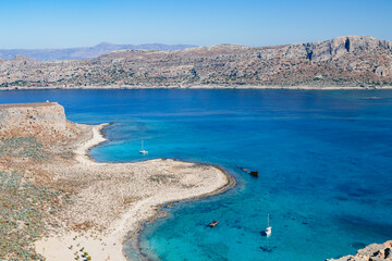 The yacht sails peacefully in the middle of the sea surrounded by mountains under a clear blue sky. Crete. Greece. Balos. The sea is azure-colored