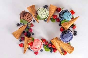 Colorful bright ice cream on bowls, with waffle cones and berries, on white background. Variety of ice cream portions with different flavor with fresh berries top view copy space layout background