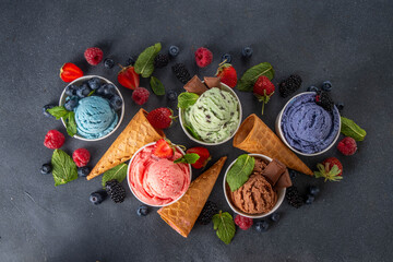 Colorful bright ice cream on bowls, with waffle cones and berries, on black background. Variety of...
