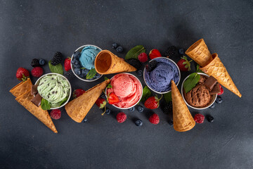 Colorful bright ice cream on bowls, with waffle cones and berries, on black background. Variety of ice cream portions with different flavor with fresh berries top view copy space layout background