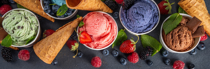 Colorful bright ice cream on bowls, with waffle cones and berries, on black background. Variety of ice cream portions with different flavor with fresh berries top view copy space layout background