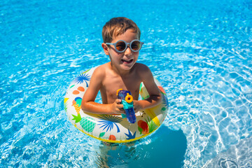 Boy aims with a water gun while playing with a float