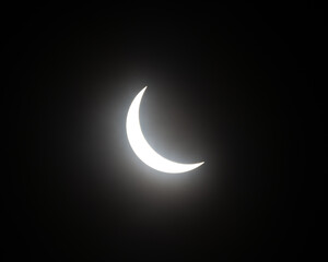Partial solar eclipse with moon blocking sun, sun shining in a crescent shape in black sky