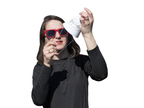 A young woman in red eyeglasses puts on a hat for birthday party isolated