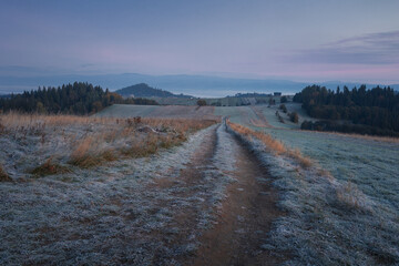 A beautiful autumn landscape of the Tatra Mountains seen from Polish Podhale during the golden hour. The sky is painted in warm hues, with the mountains bathed in golden light.