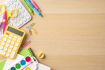 Top view of colorful school supplies including calculator, scissors, pens, paper clips, and watercolor set on a wooden desk with copy space