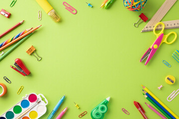 Assorted colorful school supplies such as pens, scissors, and paper clips on a green background arranged for back to school theme