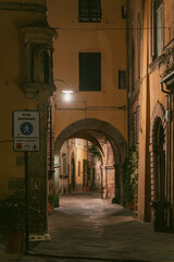 A quiet, narrow street in Lucca, Italy at night with warm lighting and historic architecture.