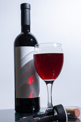 There is a bottle of wine positioned beside a glass of wine on the table