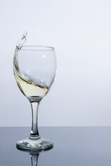 A glass of white wine with a splash emanating from it on the table