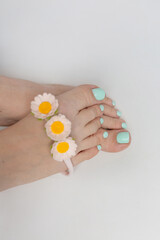 female legs. mint pedicure. female legs on a white background with daisies
